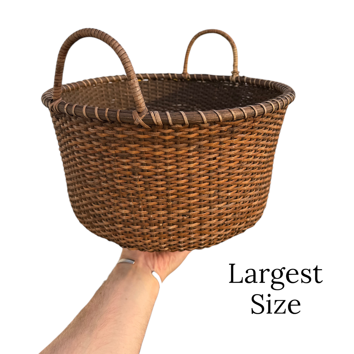 Large woven rattan produce basket with two loop handles, held by hand