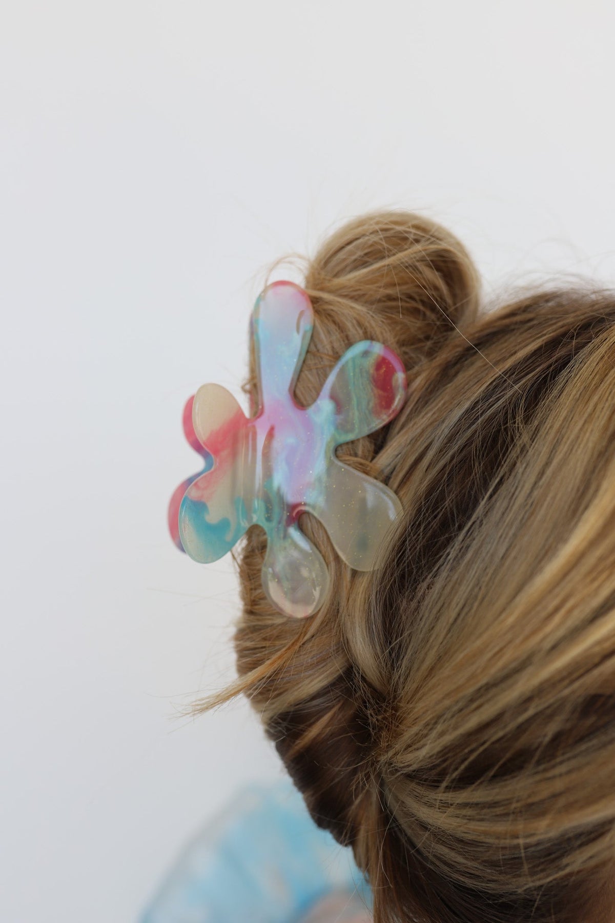 Iridescent flower-shaped hair claw securing blonde bun, close-up side