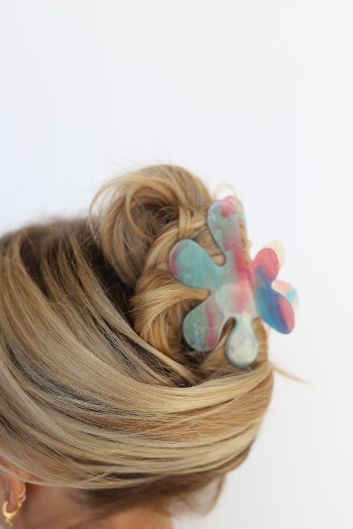 Flower-shaped iridescent hair claw clipped in blonde hair, side view updo