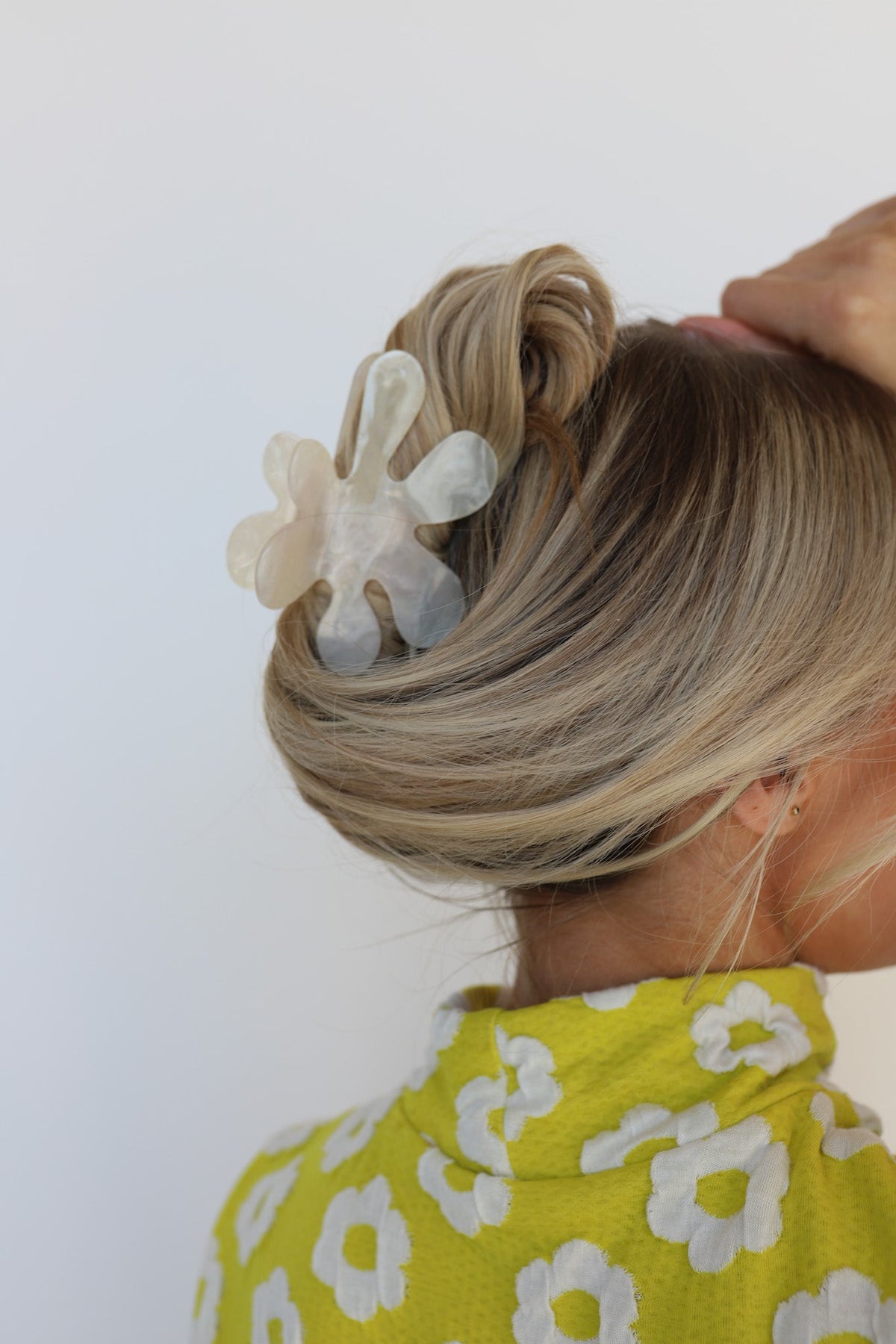 Translucent white flower hair claw clipped in blonde updo, hand adjusting
