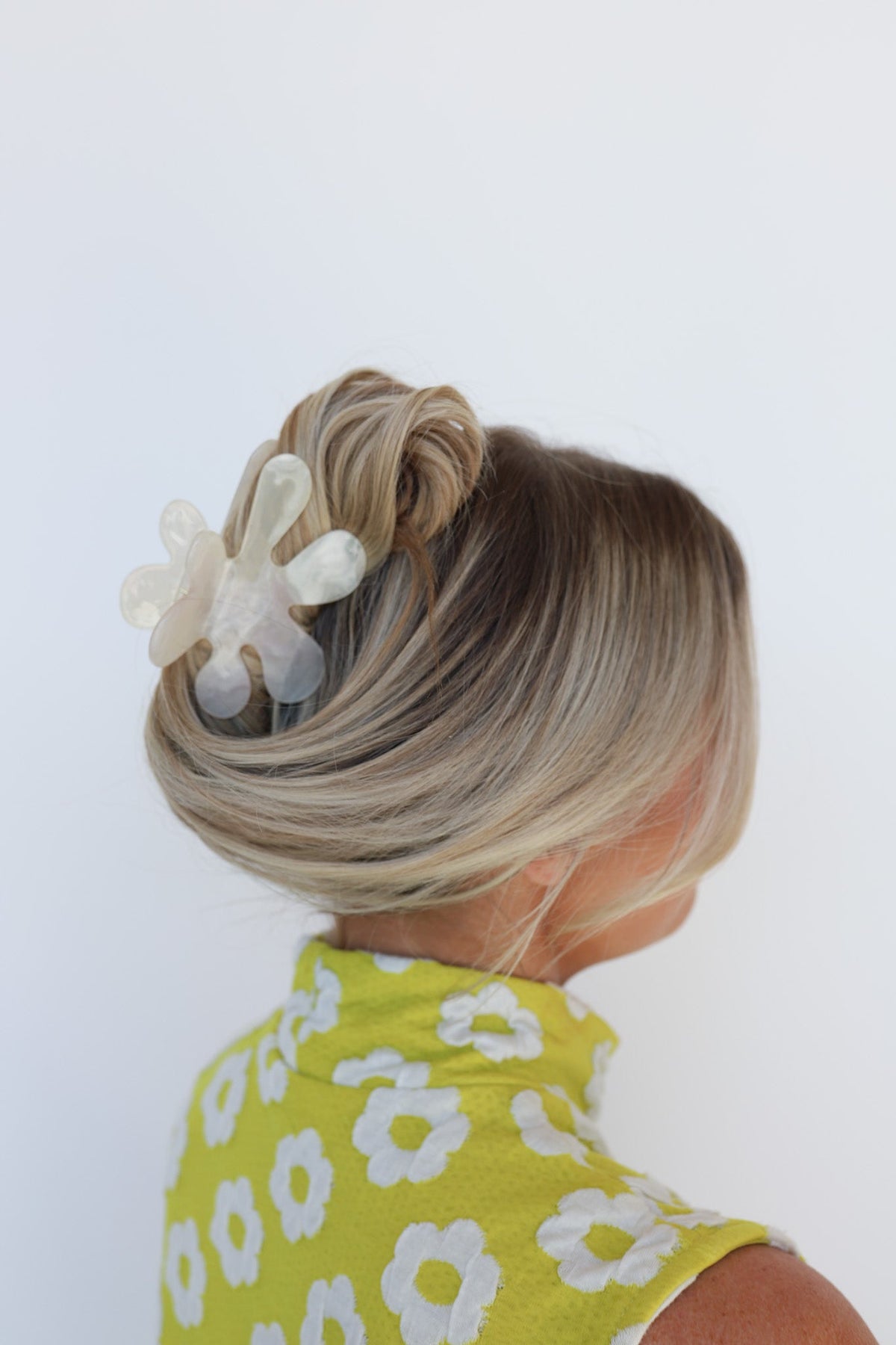 White flower hair claw on blonde bun, view from behind with yellow dress