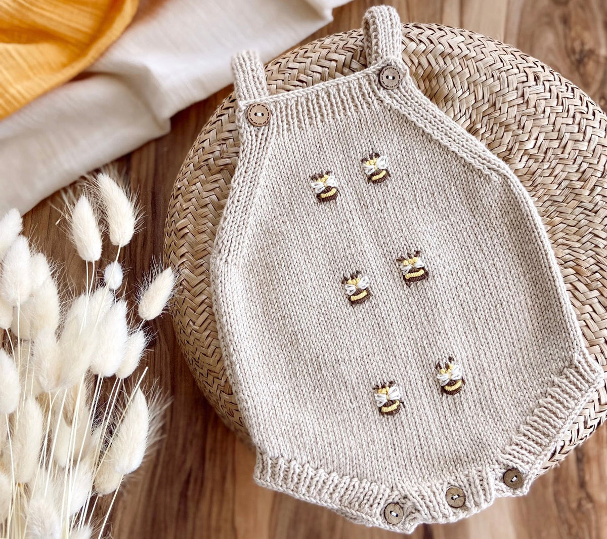 Light beige knit baby romper with snap buttons and bee appliques