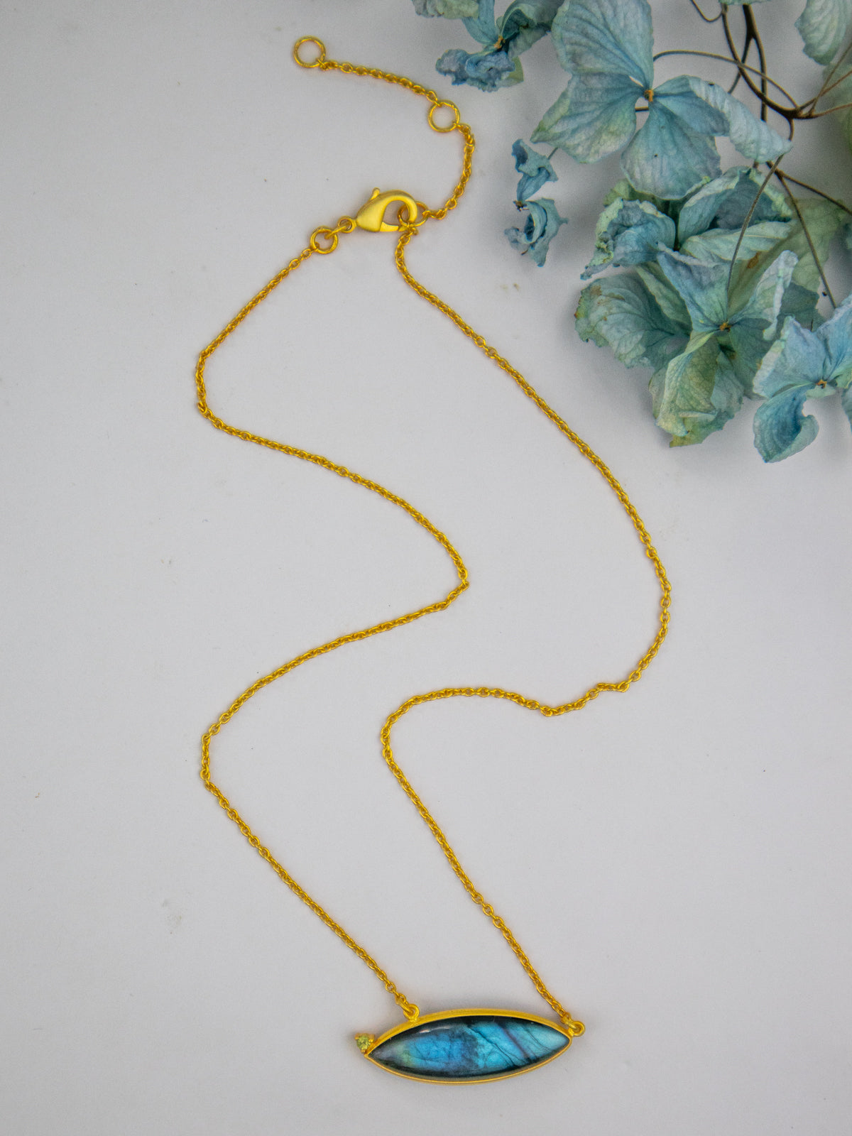 Gold beaded chain necklace with oval blue pendant lying flat