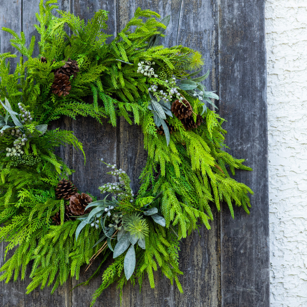 Green evergreen wreath featuring pinecones and frosted berry clusters