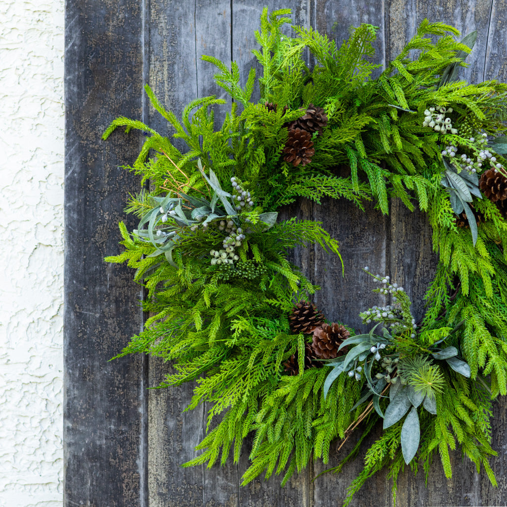 Green evergreen wreath with pinecones, frosted berries, and pale blue leaf sprigs