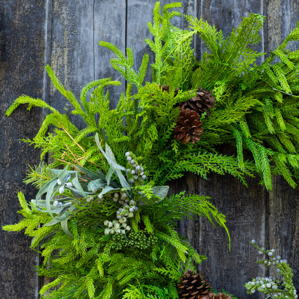 Green evergreen wreath with pinecones and frosted berry clusters on dense foliage