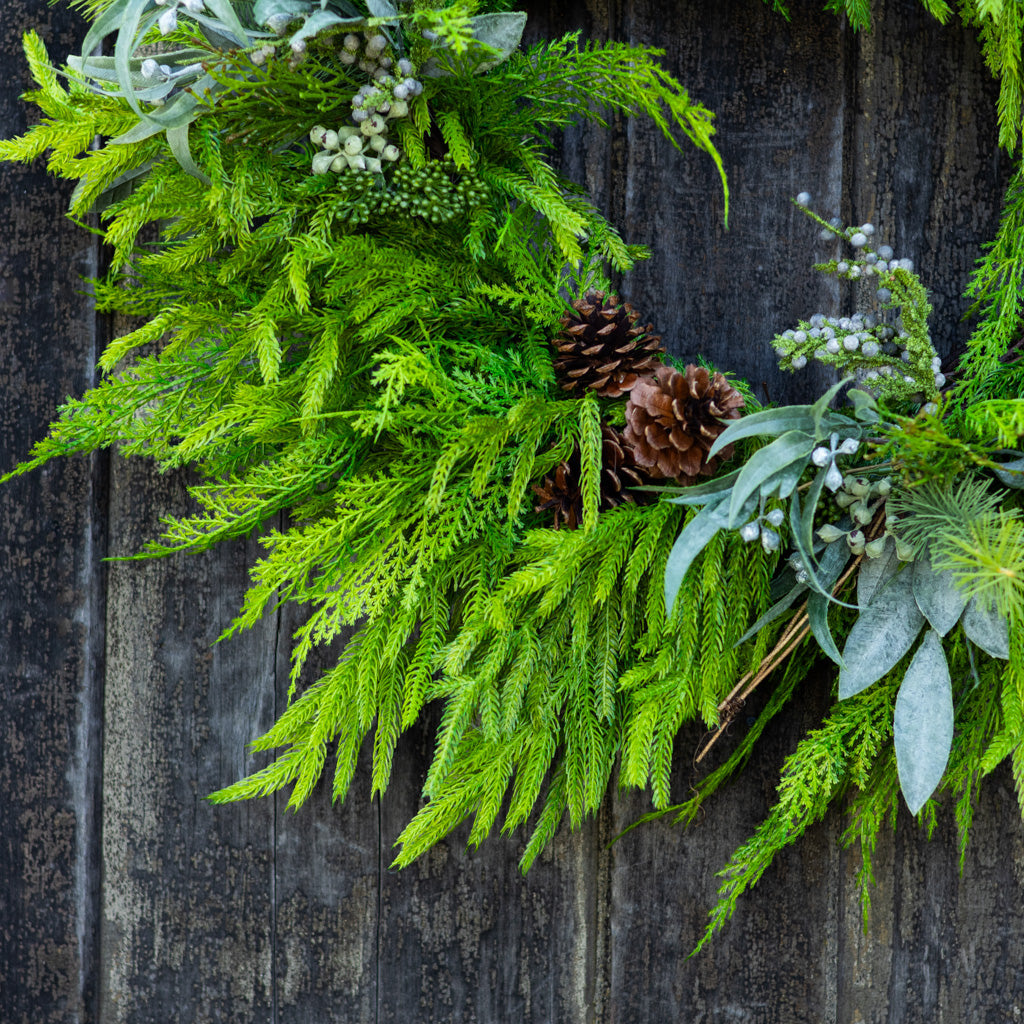 Close-up green evergreen wreath with pinecones, bead berries, and gray-blue leaves