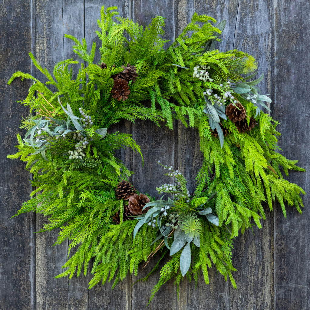 Green evergreen wreath with pinecones, frosted berries, and pale blue leaves