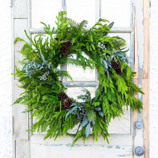Green evergreen wreath with pinecones, bead-like berries, and blue-gray leaf accents