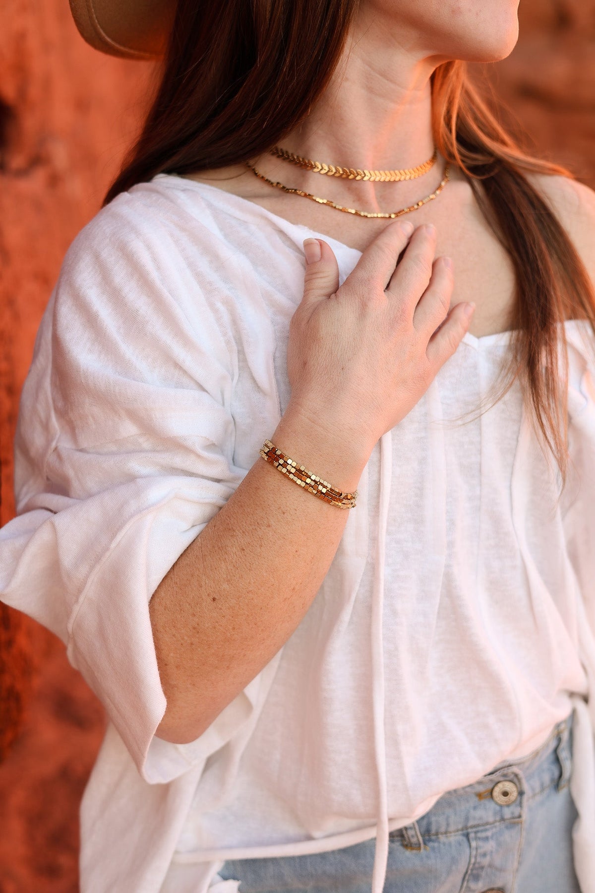 Gold Ember bracelets stacked on a wrist, with delicate chain and bead details.