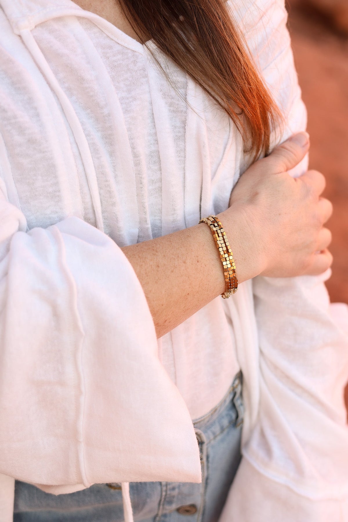 Gold Ember bracelets with square beads worn as a layered stack