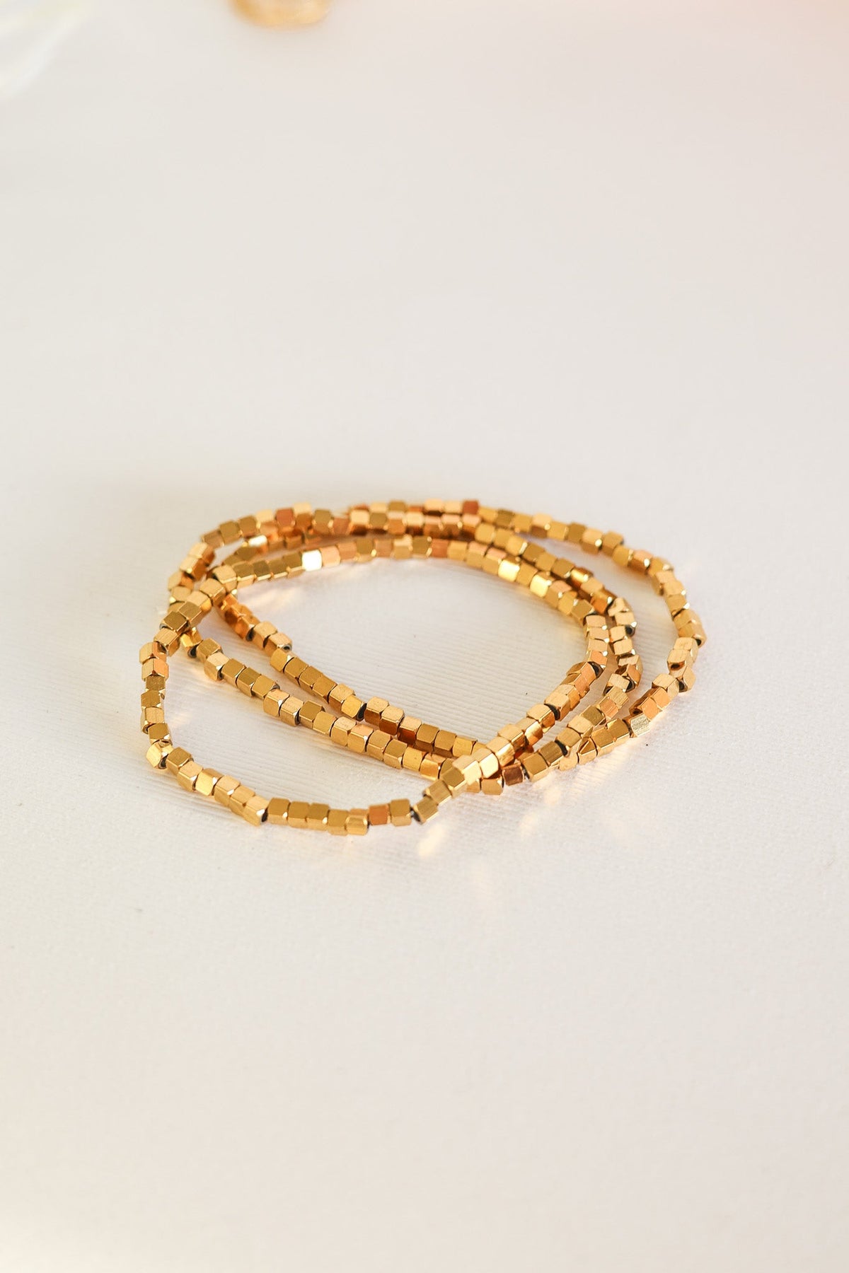 Ember gold bracelets with small square beads, shown as a layered set