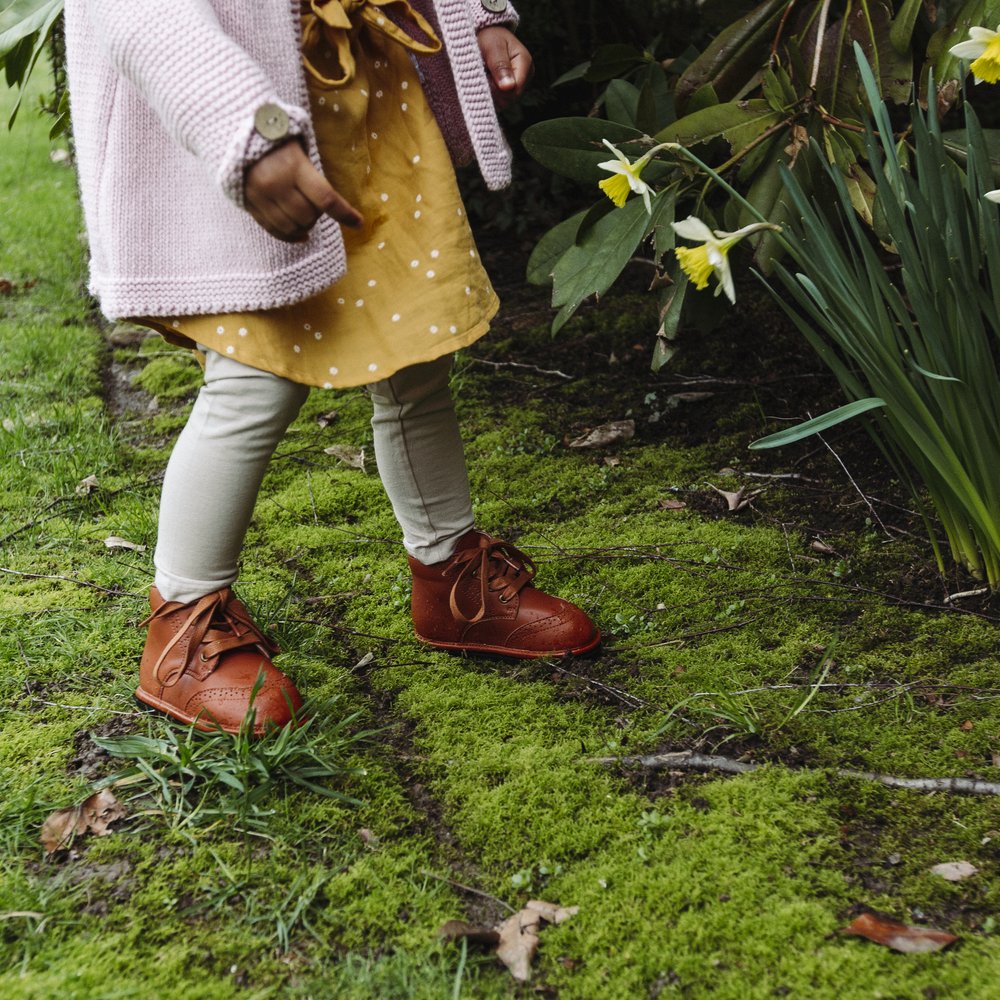 Kids chestnut lace-up boots worn on green grass outdoors.