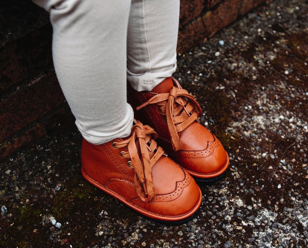 Kids lace-up chestnut boots worn outdoors on a paved walkway.