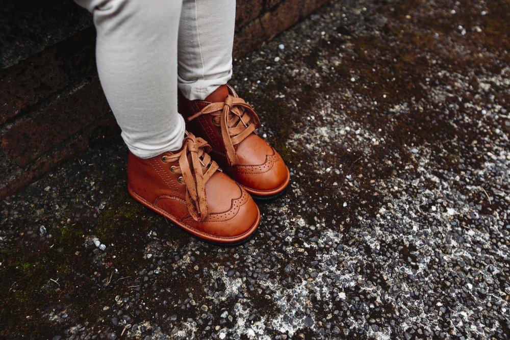 Kids chestnut lace-up boots on gravel, stitched toe and laces visible.
