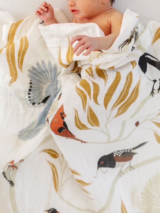 Swaddle blanket covering a baby, featuring printed birds and leafy branches on white