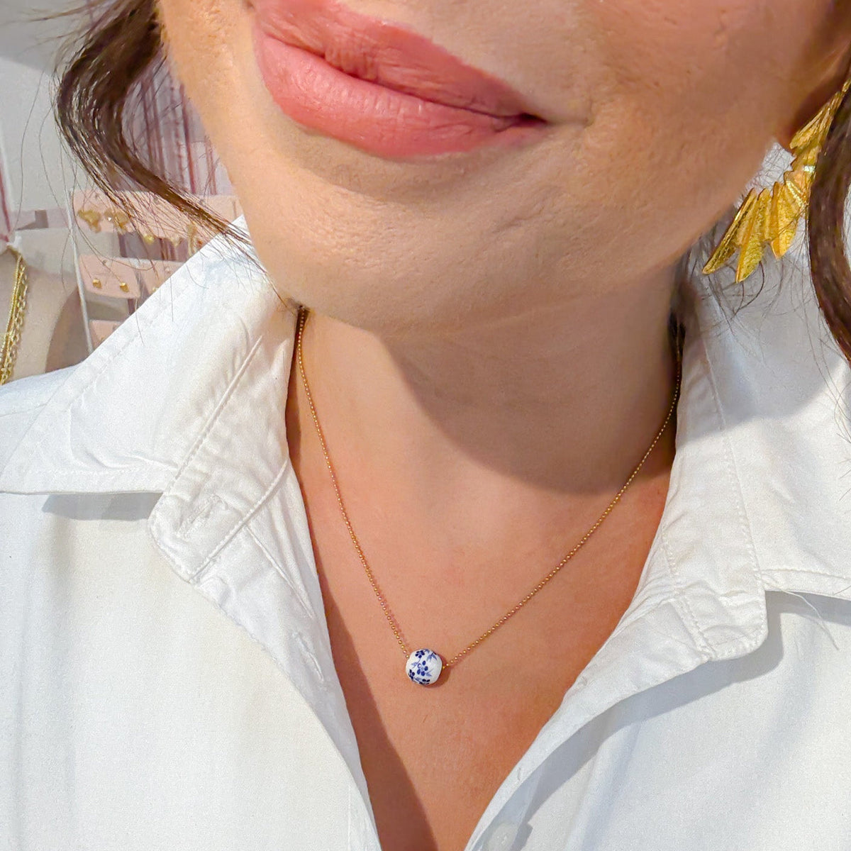 Gold bead necklace worn with a small round blue-and-white floral pendant.