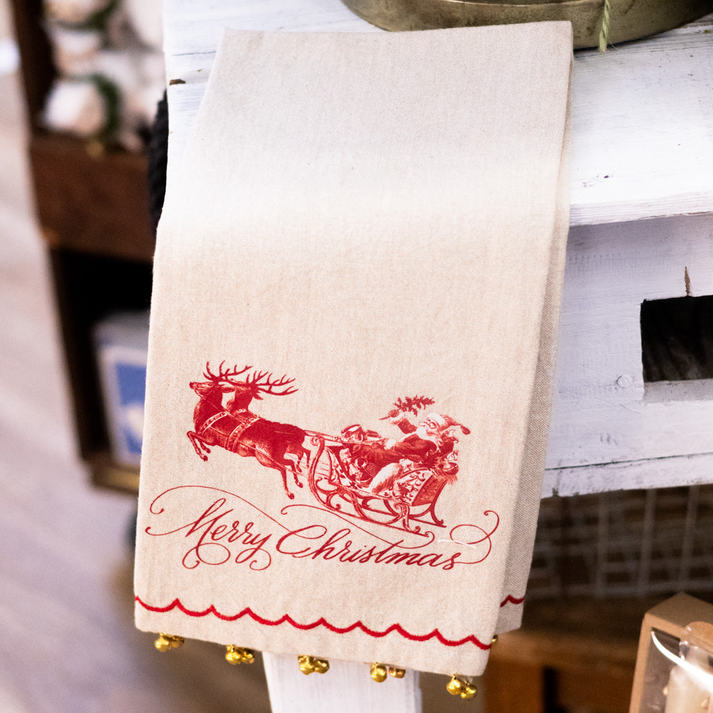Beige Christmas hand towel with red Merry Christmas text, Santa sleigh print, bell trim