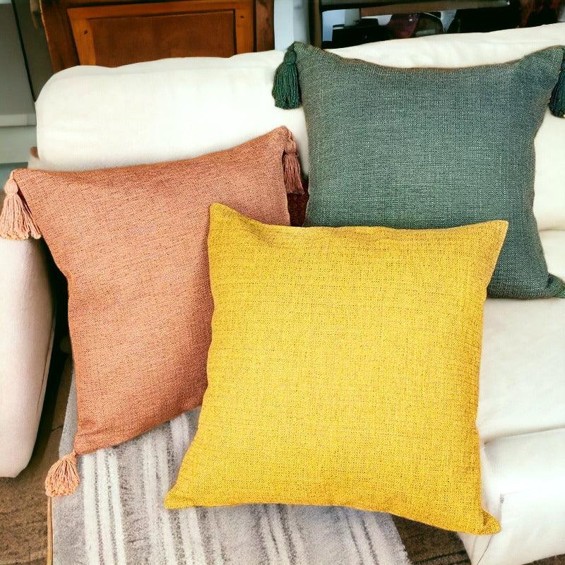 Square pillow covers in deep green, bright yellow, and dusty rose on a couch