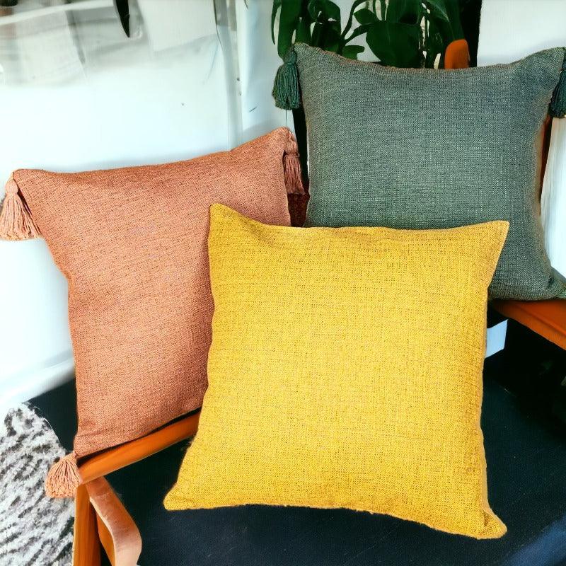Decorative square pillow covers in dusty rose, bright yellow, and deep green with tassels