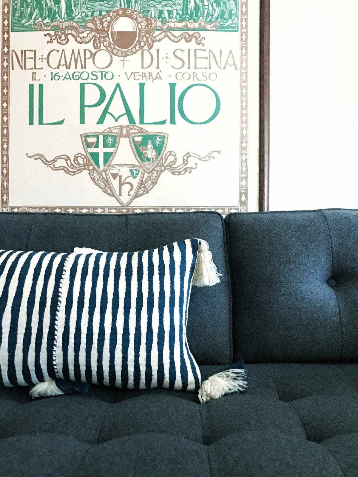 Dark teal striped pillow with corner tassels on a sofa