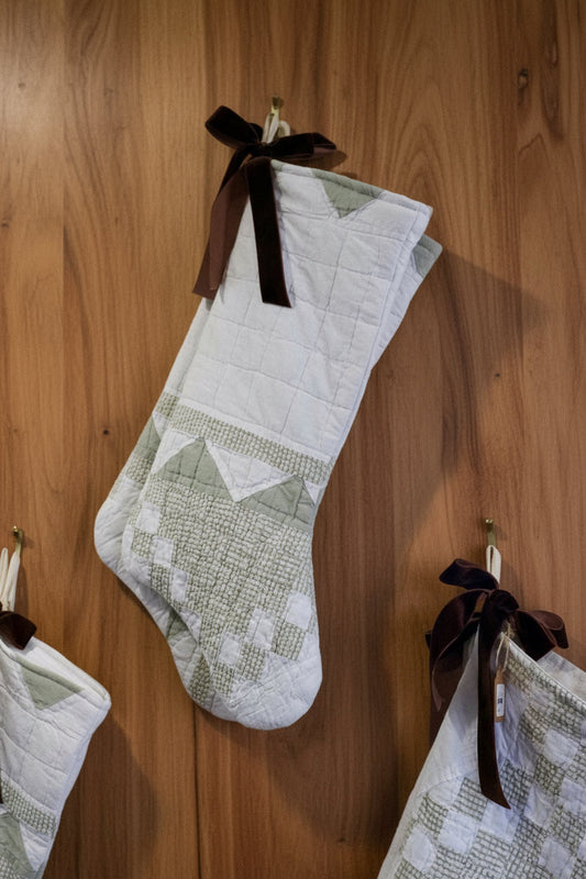 Quilted holiday stocking with patchwork blocks, white fabric, and dark ribbon loop.
