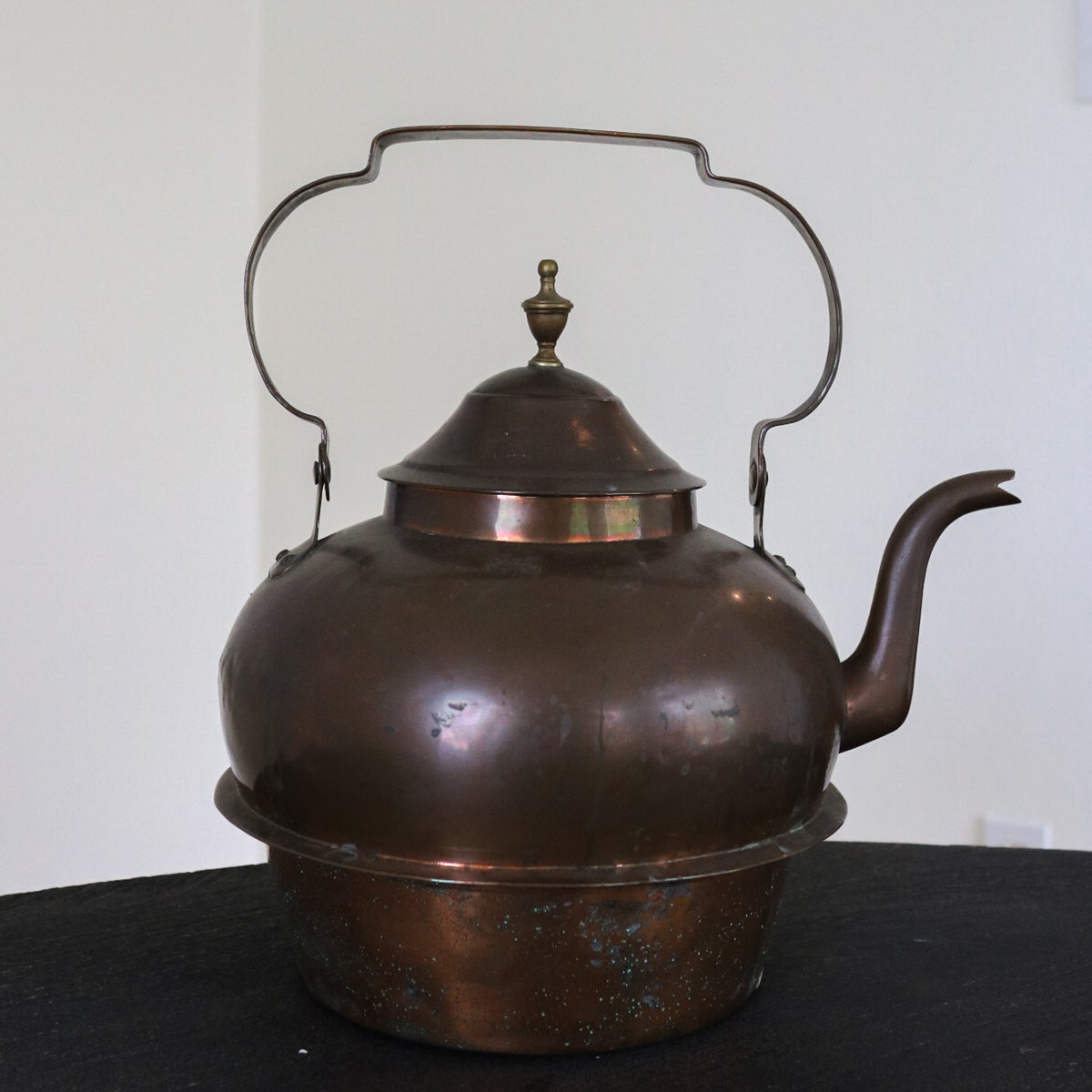 Brass and copper kettle with dark domed lid, arched handles, and curved spout