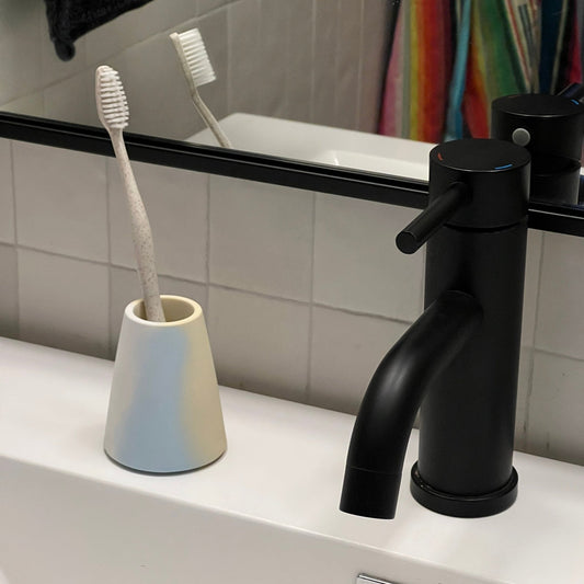 Light blue ceramic toothbrush holder with two upright toothbrushes on bathroom counter