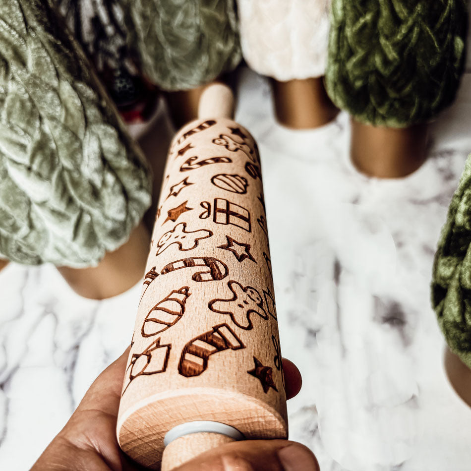 Hand holding a wooden rolling pin with dark engraved house and tree icons