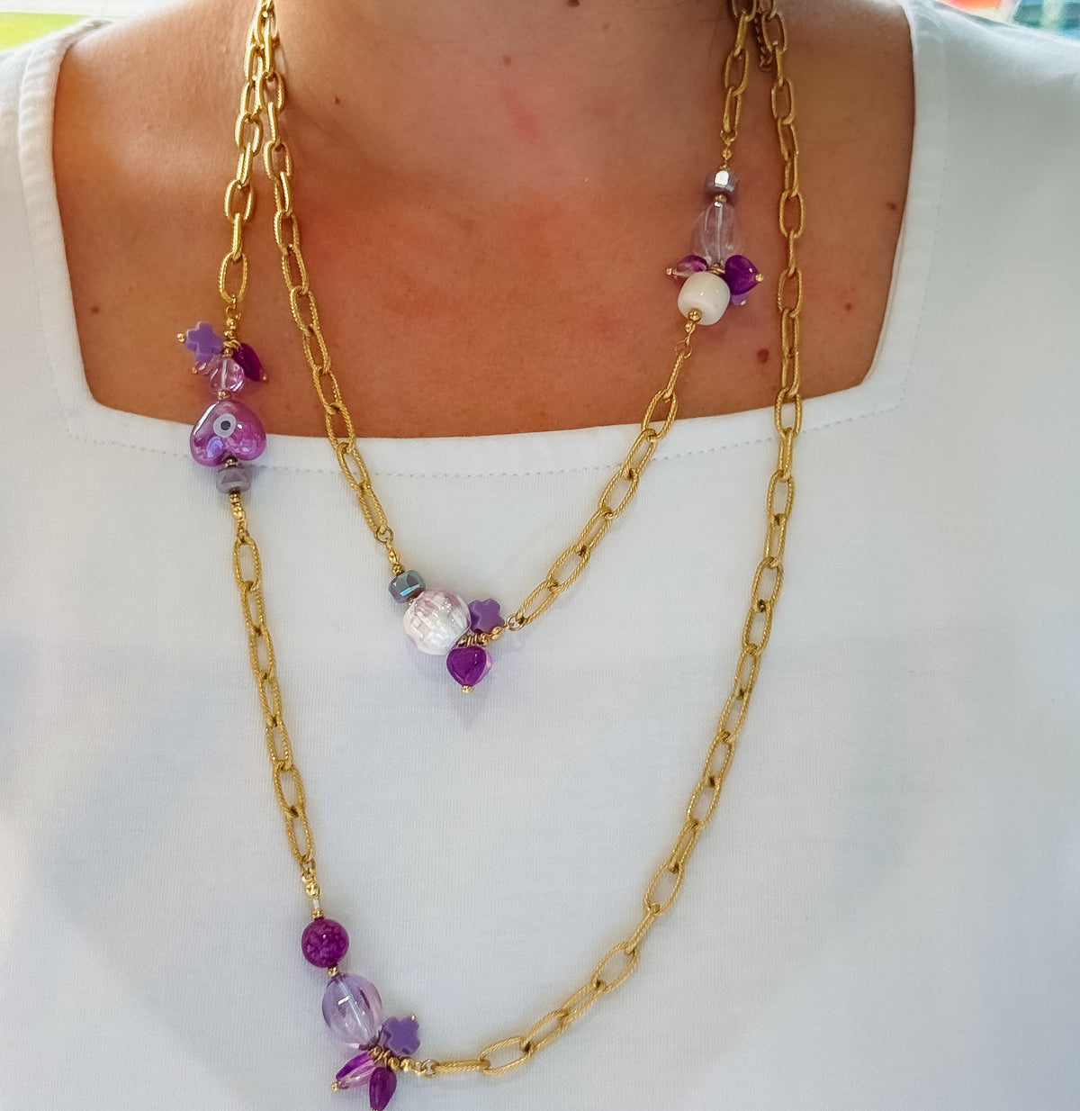 Layered gold necklace worn on model with purple bead and flower charms, long chains