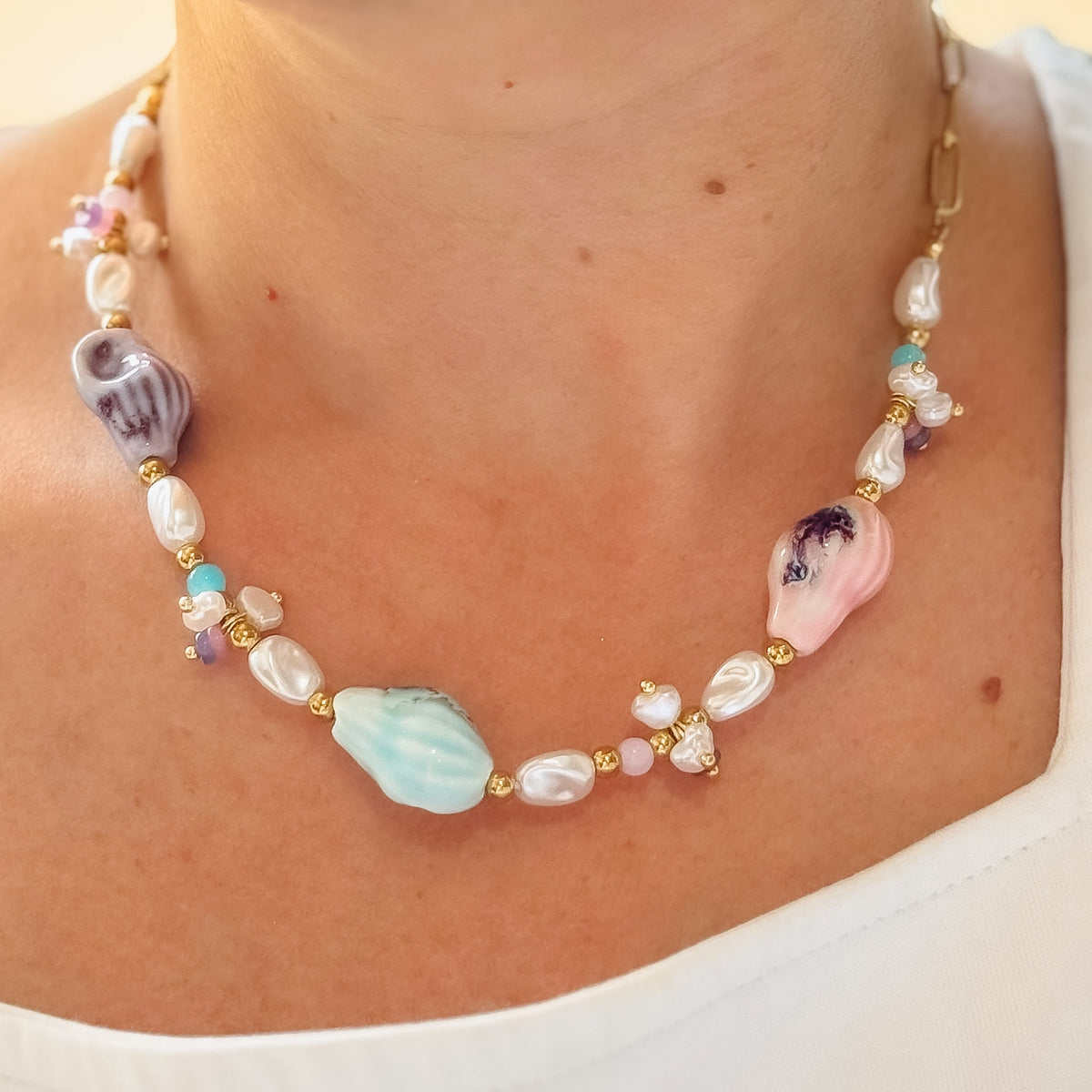 Pastel beaded necklace close-up with pearl beads, gold accents, and pink shell centerpiece