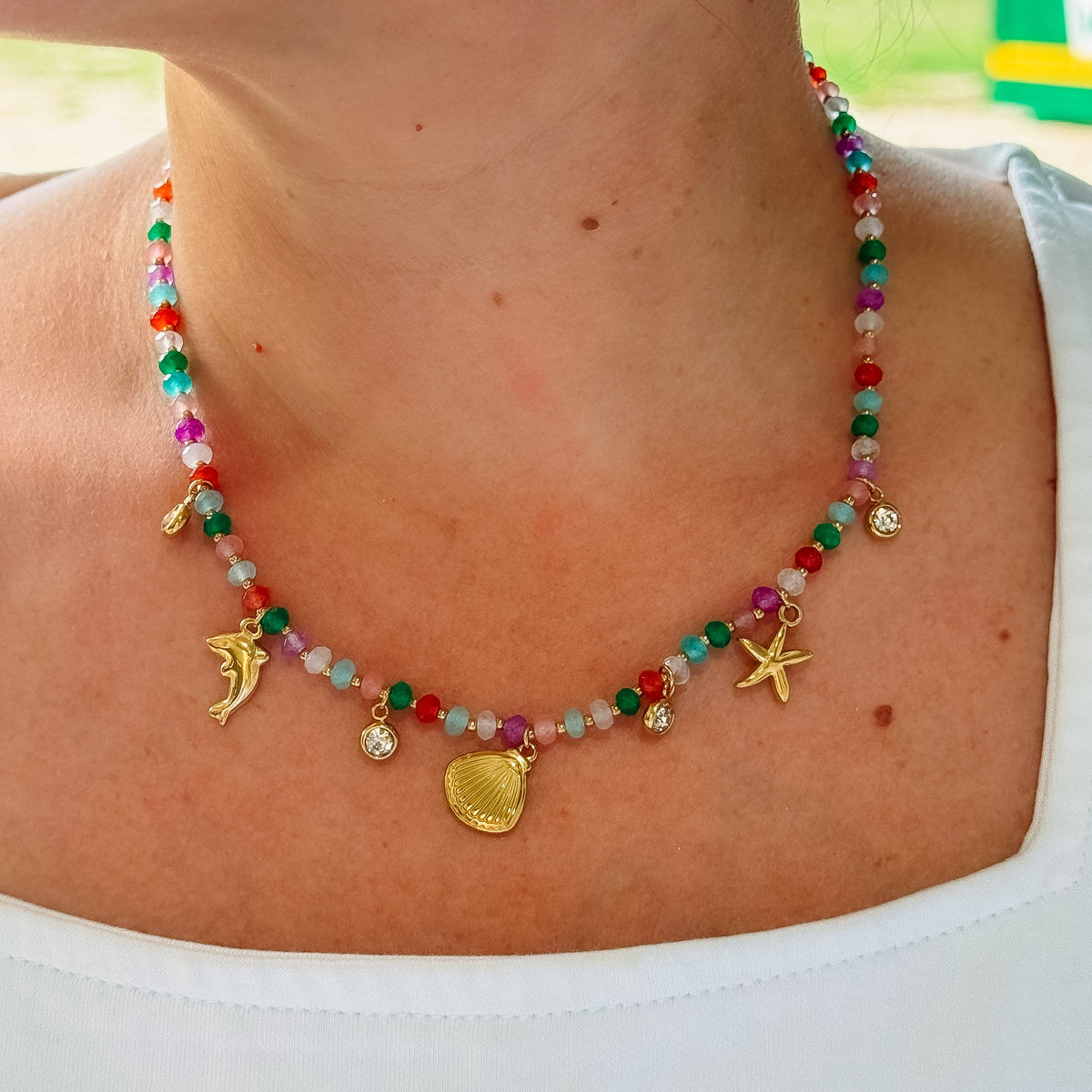 Beaded charm necklace worn on neck with shell, starfish, dolphin and crystal accents