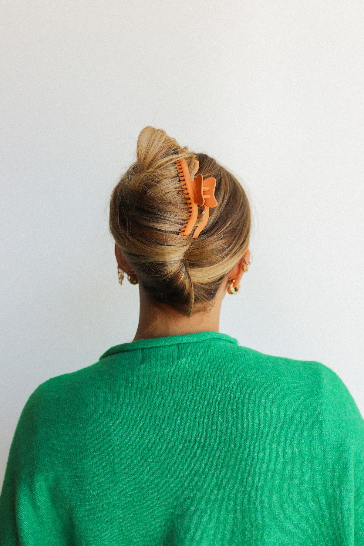 Wavy hair claw clip in warm orange, holding blonde hair in a neat bun