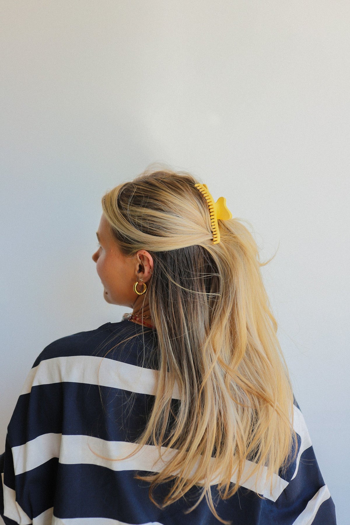Wavy hair claw clip holding blonde hair in a half-up bun, yellow