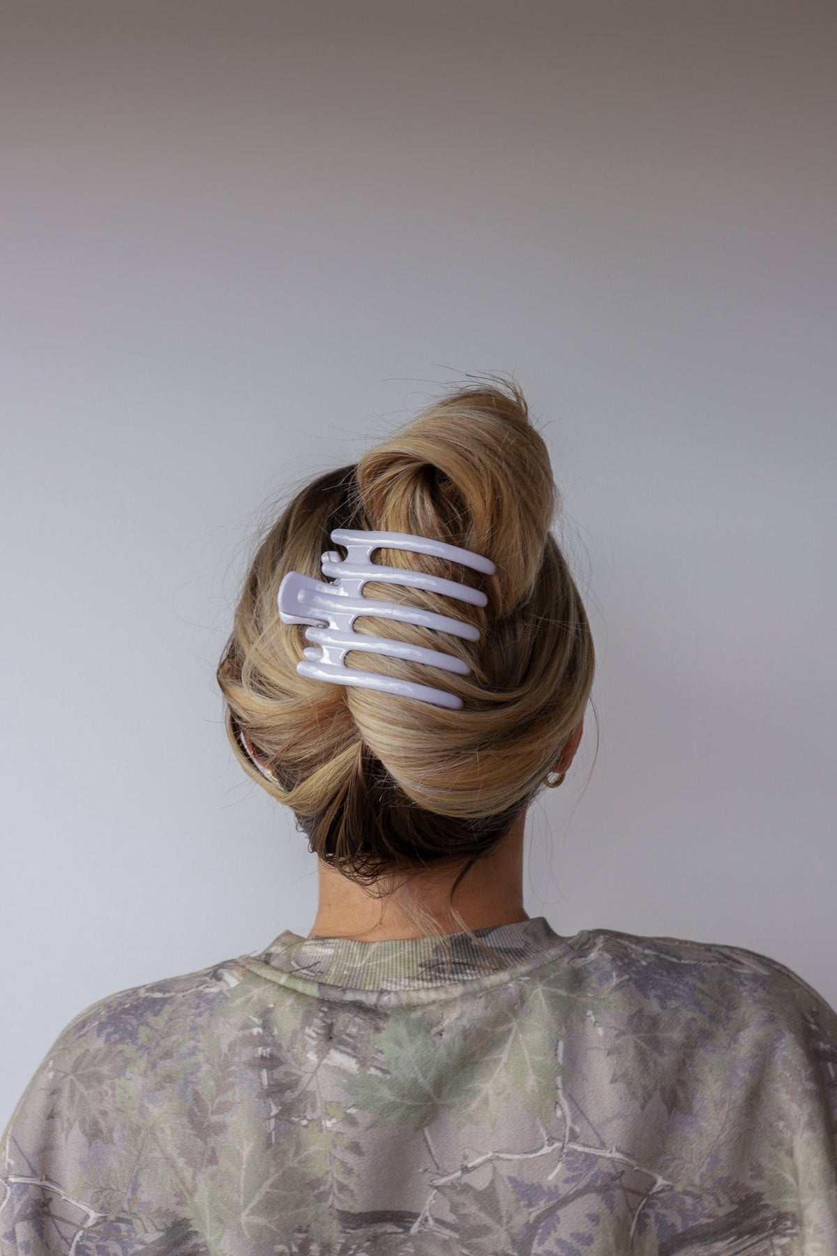 Wide lay-down hair claw, glossy white; secures hair into a rounded bun