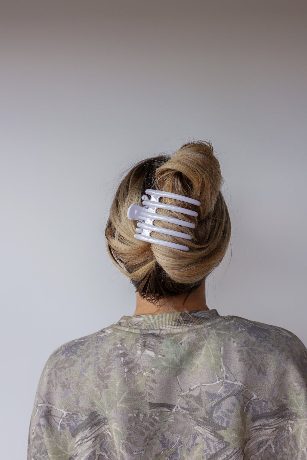 Wide lay-down hair claw, matte white; clips blonde hair into a back bun