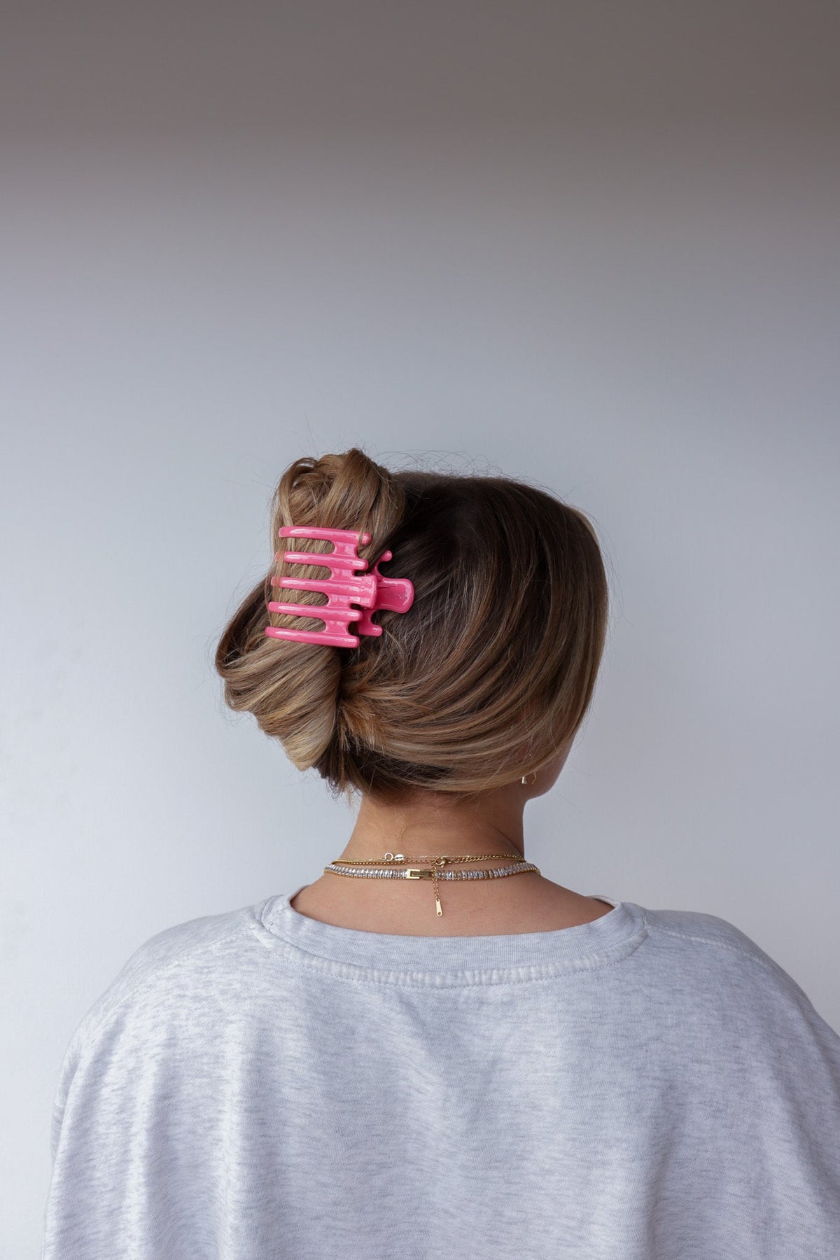 Wide hot-pink hair claw with five teeth clipped in dark hair, back view