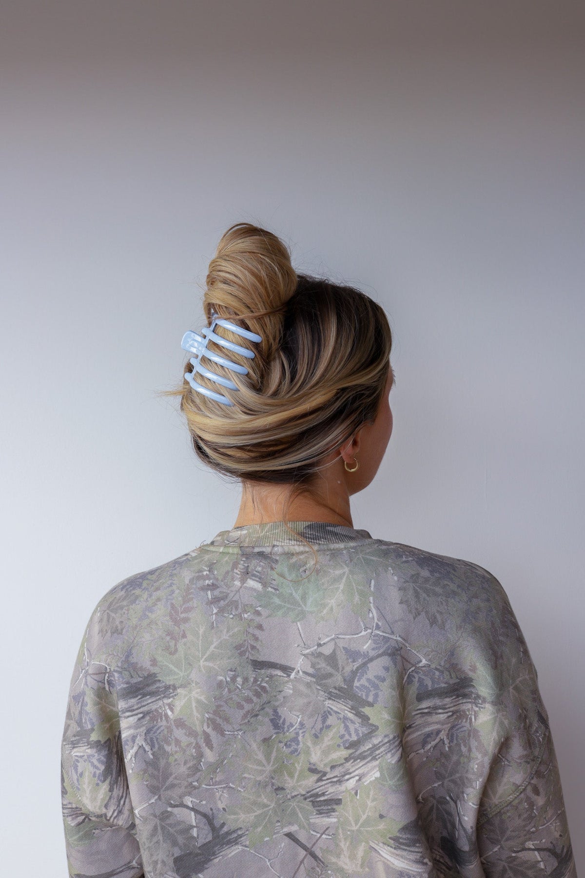 Wide lay-down claw hair clip in hair, glossy light blue with claw tines.