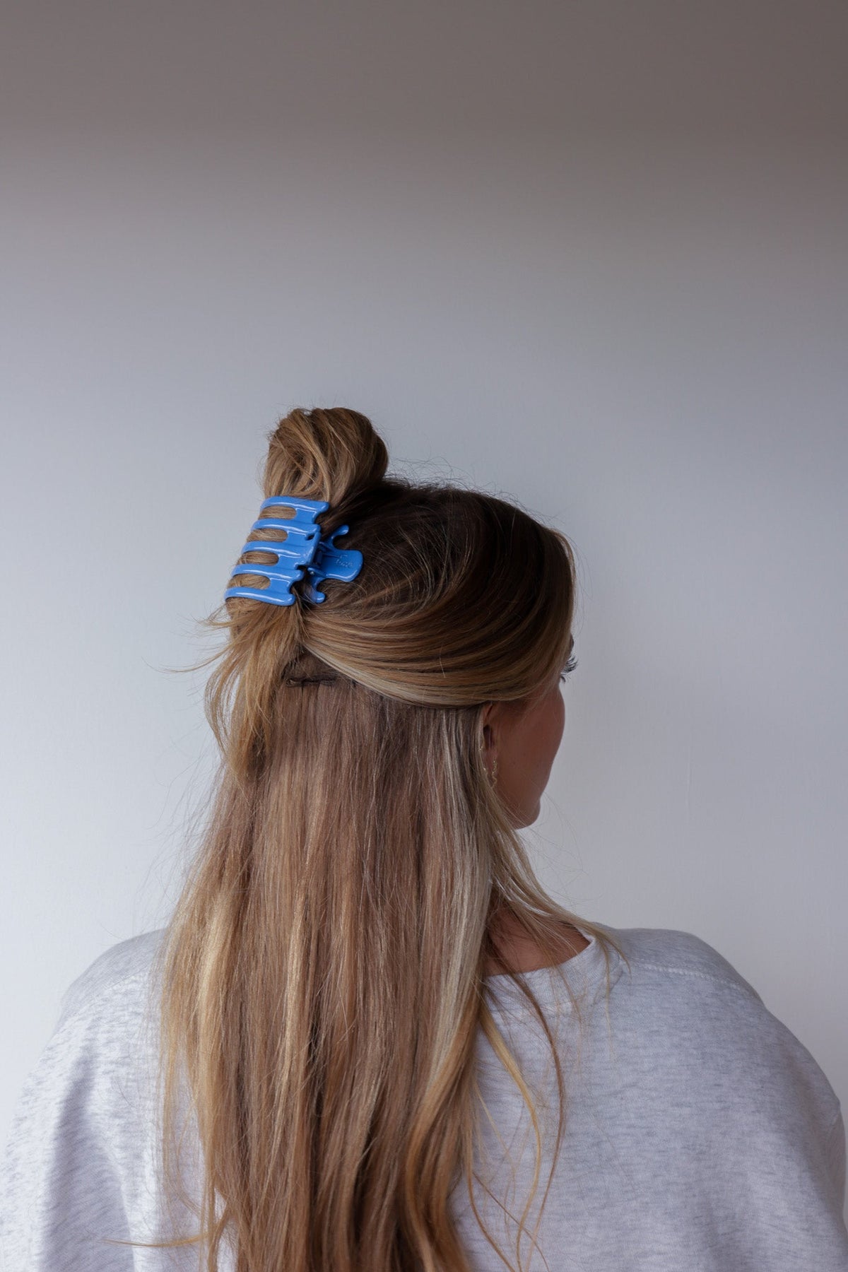 Wide lay-down claw hair clip, glossy bright blue, holds high ponytail section.