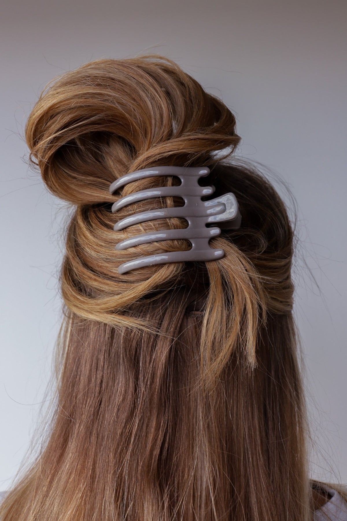 Wide lay down hair claw in shiny light gray, holding hair in an updo.