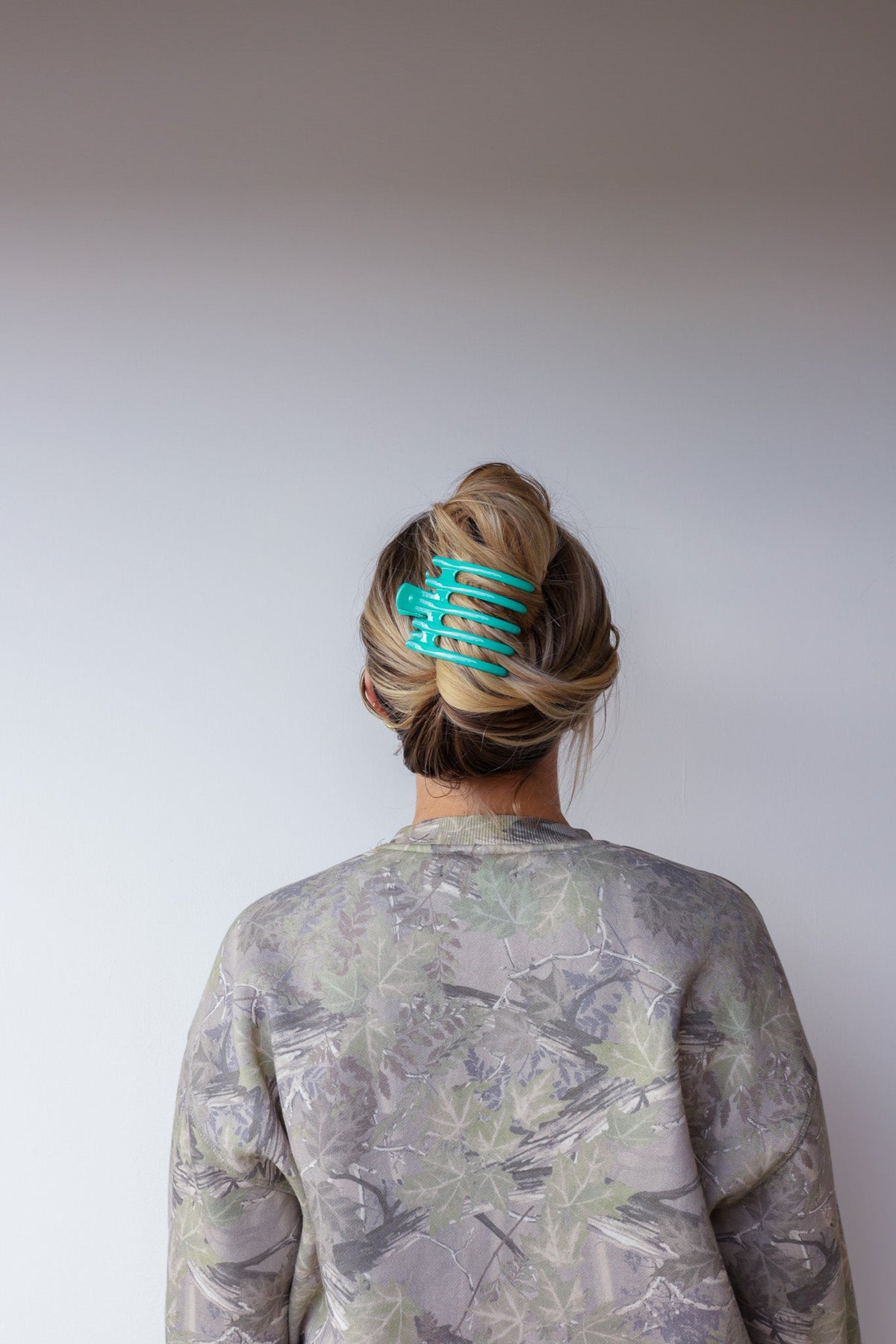 Wide lay-down hair claw, glossy teal; holds hair bun at the back of the head
