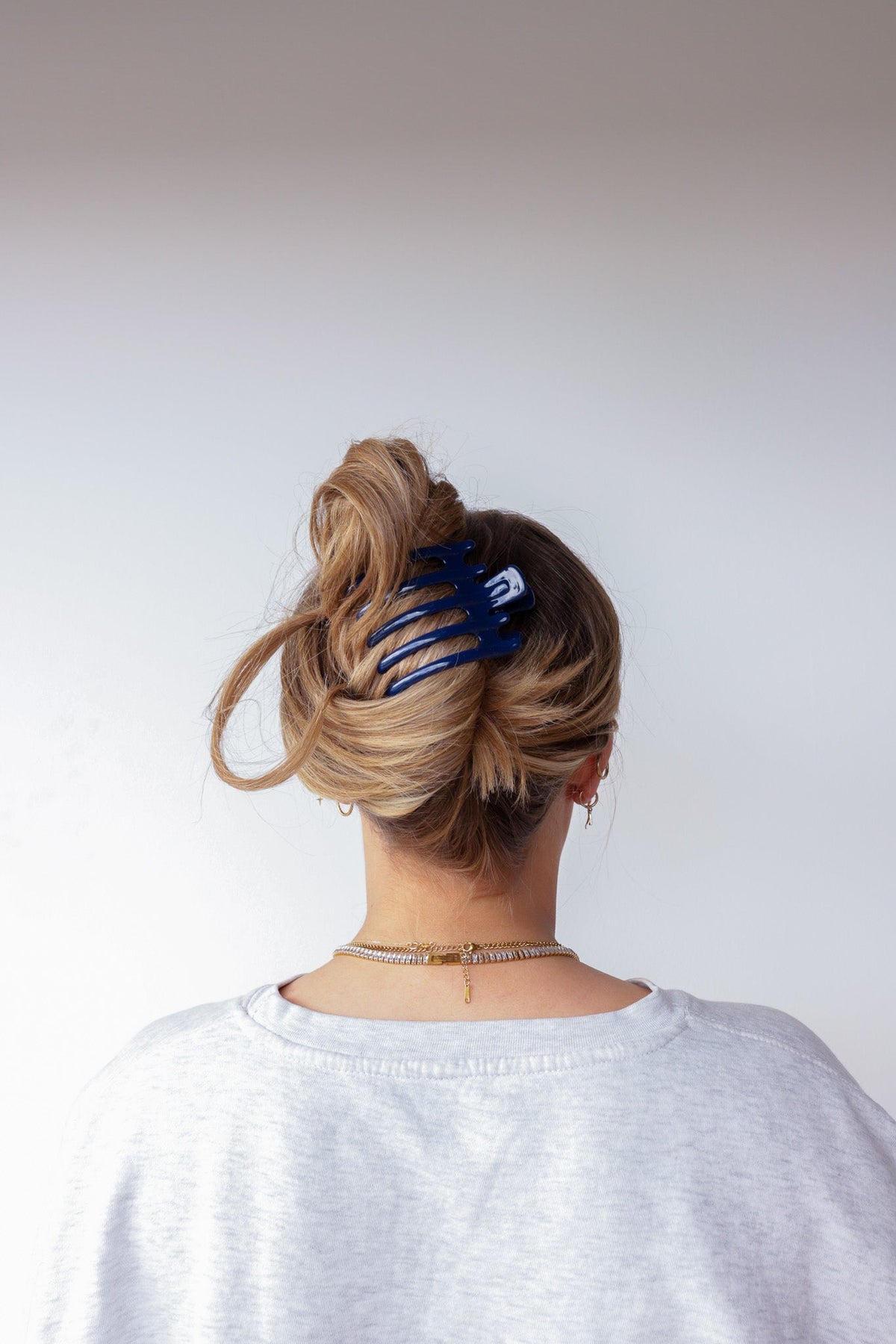 Wide lay-down claw hair clip in bun, glossy deep navy blue, wide teeth.