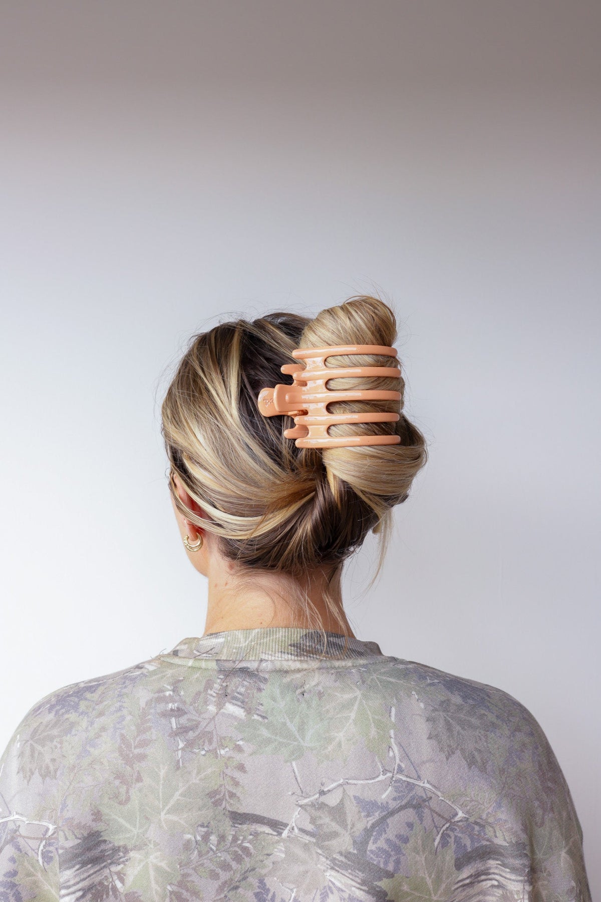Wide lay-down hair claw, shiny orange; holds hair in a high twisted bun