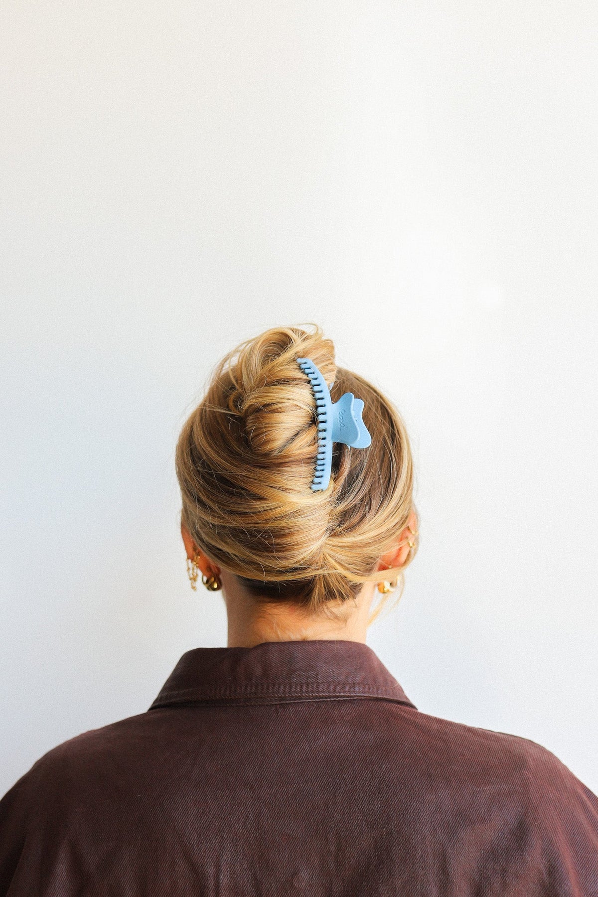 Wavy hair claw clip holding blonde hair bun, gold with blue accent
