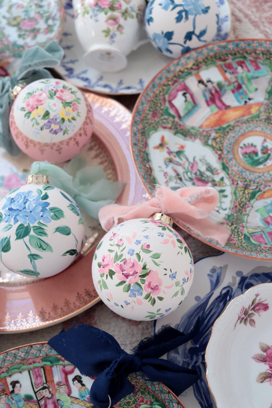 Round white ornament with hand-painted pink roses and green leaves, displayed with a pink bow