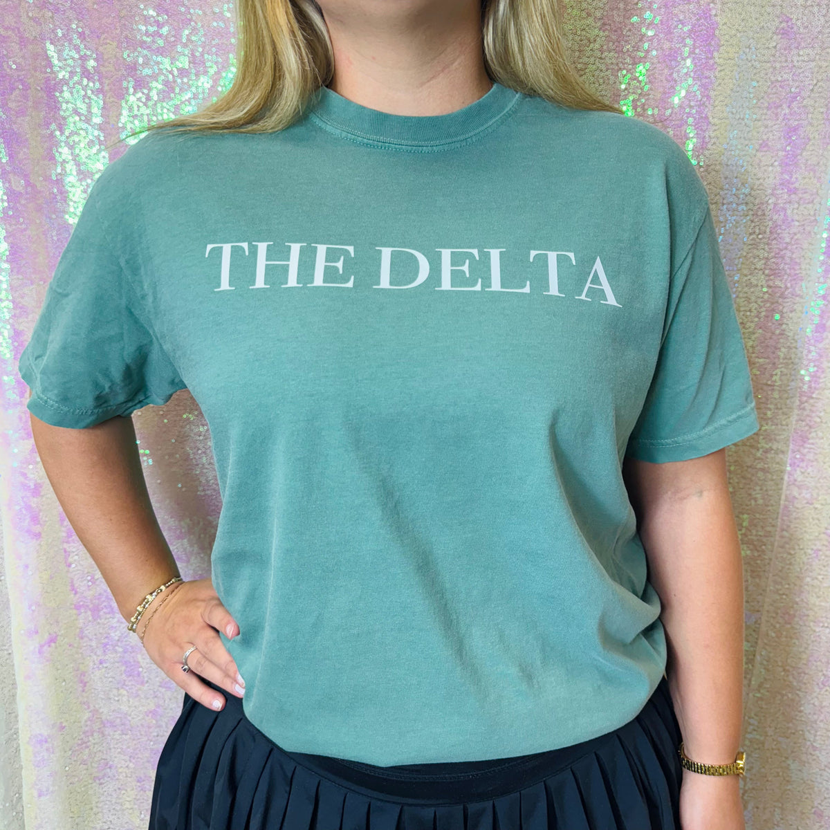 Teal crew-neck graphic T-shirt with white “THE DELTA” text on the chest.