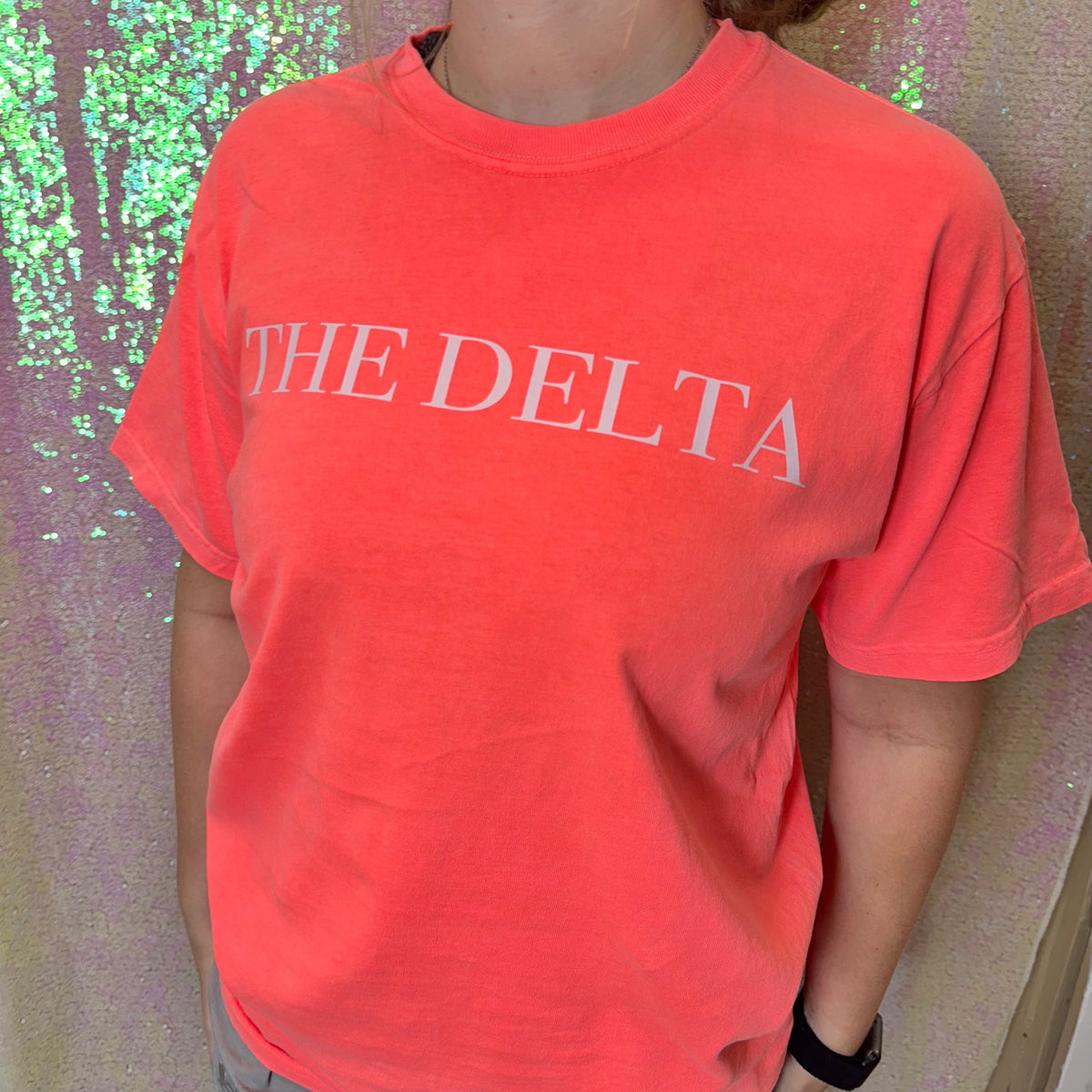 Coral/red crew-neck graphic T-shirt with white “THE DELTA” text on the chest.