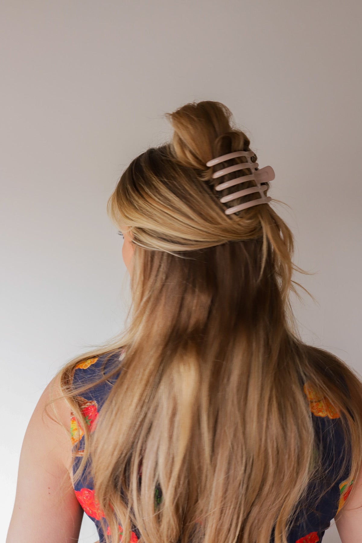 Wide lay down hair claw in shiny light gray, securing long blonde hair.