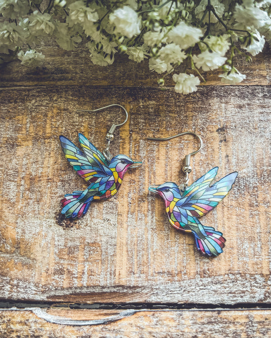 Pair of colorful hummingbird dangle earrings with silver hooks on wooden background.