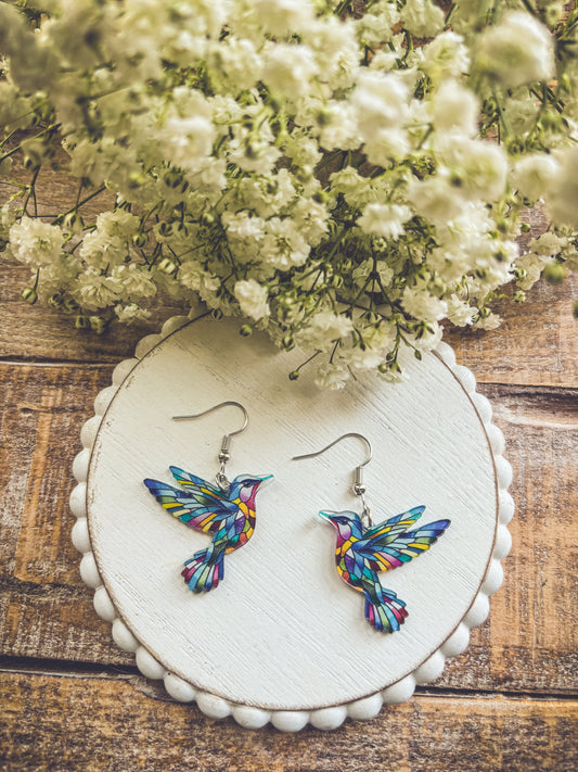 Colorful hummingbird dangle earrings with silver hooks on round display card.